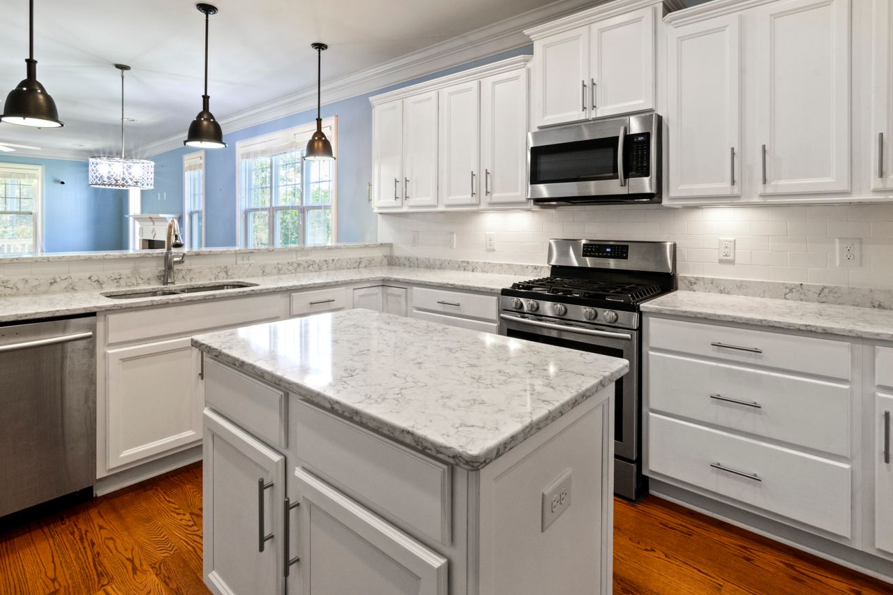 A bright, spacious kitchen with marble countertops, stainless steel appliances, and elegant white cabinetry.